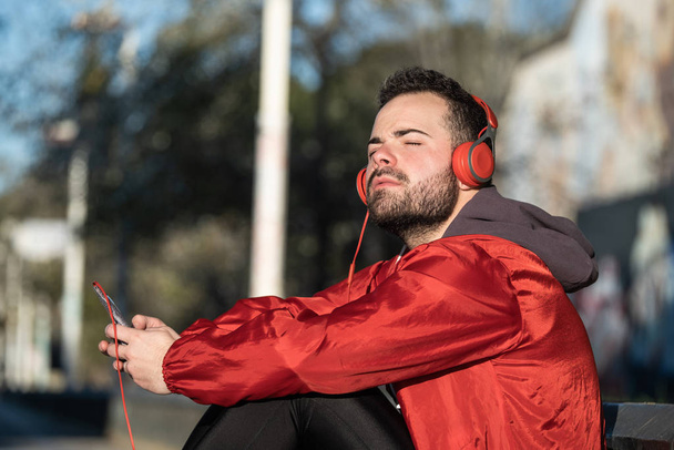 joven en ropa deportiva escuchando música con un par de auriculares
 - Foto, Imagen