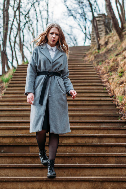 A young girl in gray coat goes down stairs in park on an autumn  - Φωτογραφία, εικόνα