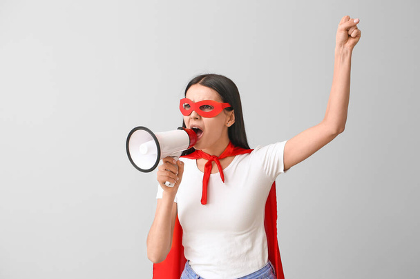 Screaming woman in superhero costume and with megaphone on grey background. Concept of feminism - Fotoğraf, Görsel