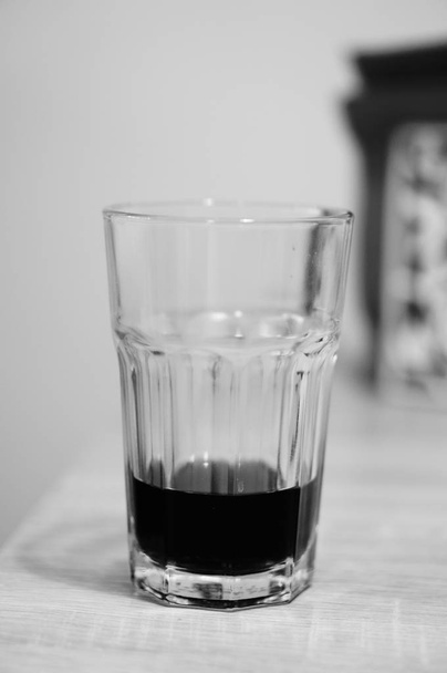 A vertical greyscale closeup shot of a glass with a beverage on the bottom - 写真・画像