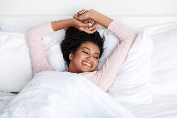 Smiling beautiful young african woman laying in bed in the morning - 写真・画像