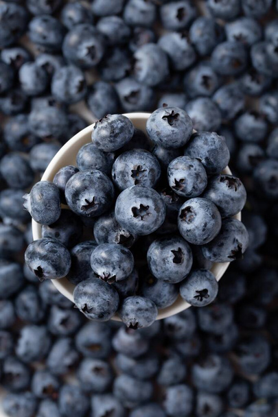 A vertical shot of a bowl of blueberries with blueberries in the background - Fotografie, Obrázek