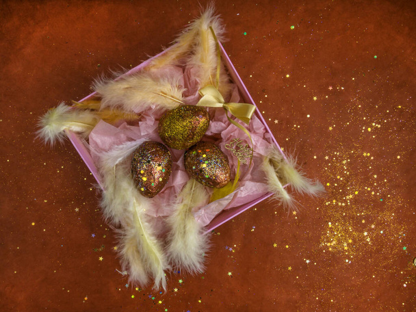 Paaseieren in een roze geschenkdoos met veren, paasversiering. Nest met gouden rode eieren op feestelijke rode achtergrond met glitters. Wenskaart. Vrolijk Pasen. - Foto, afbeelding