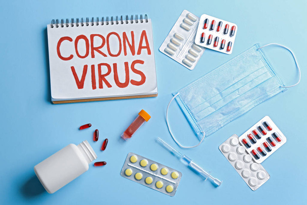 Flat lay composition of medications and notebook with words CORONA VIRUS on light blue background - Photo, image