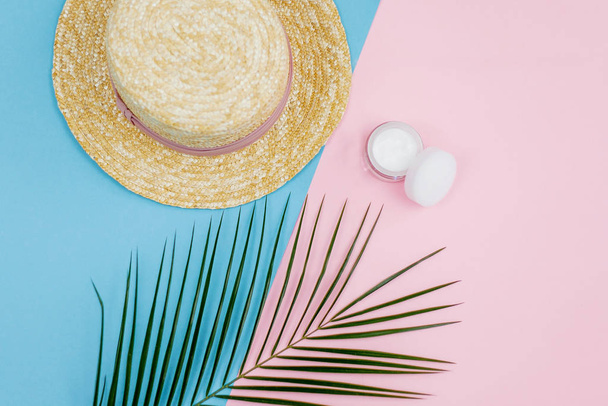 Trópusi növény, női szalma kalap, krém egy tégelyben egy kék rózsaszín háttér. - Fotó, kép