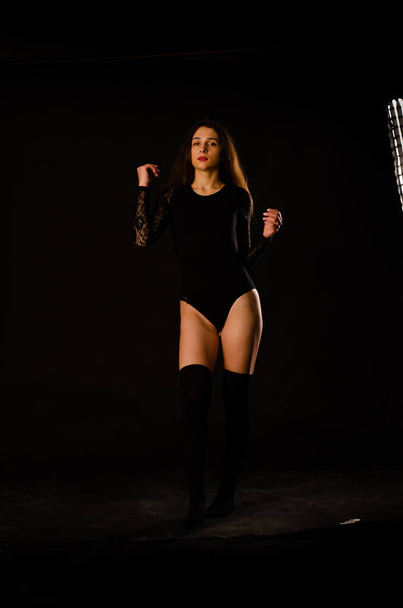 молода жінка в чорному комбінезоні позує на темному тлі, чорне волосся і м'язистої спортивної фігури
. - Фото, зображення