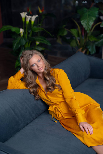 Beautiful young girl in a yellow dress on the sofa. - Photo, Image