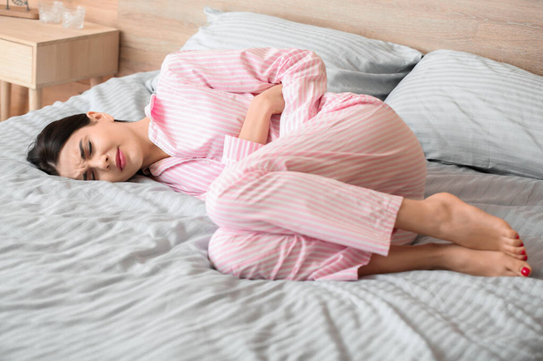 Fiatal nő szenved menstruációs görcsök a hálószobában - Fotó, kép