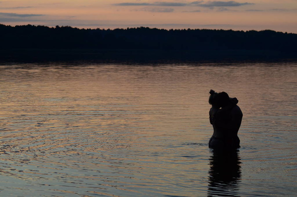 sylwetki przytulające parę nad jeziorem o zachodzie słońca - Zdjęcie, obraz