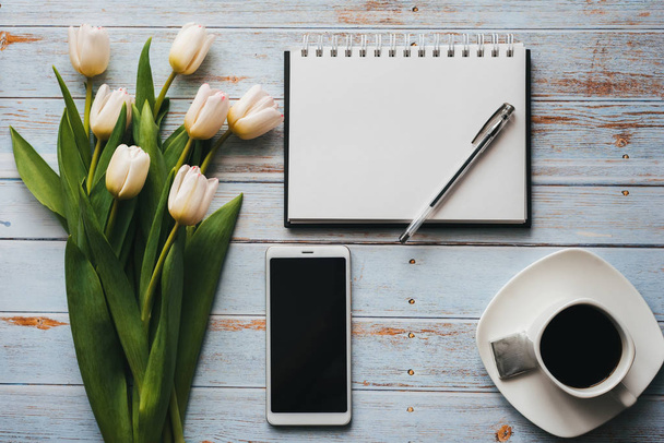 White bouquet of tulips on wooden background with coffee Cup, smartphone and empty notebook - Φωτογραφία, εικόνα