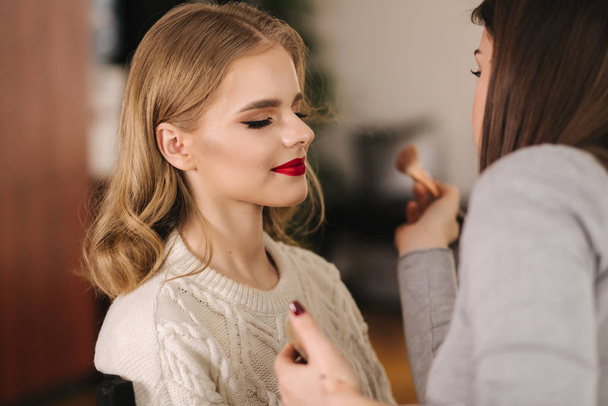 Makeup artist work in beauty studio. Woman applying by professional make up master. Beautiful make up artist make a makeup for blond hair model - Foto, afbeelding