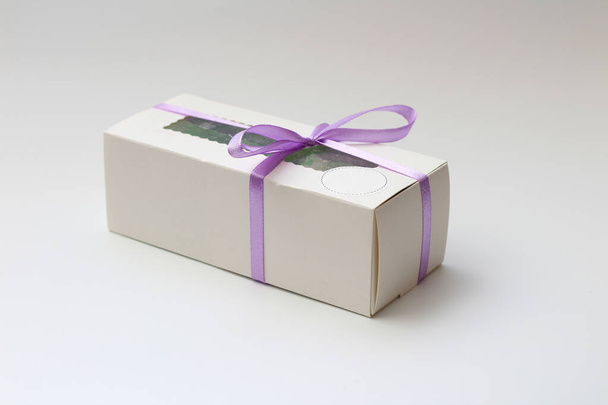 Witte kartonnen doos met een transparante bovenkant gebonden met een lila lint geïsoleerd op een witte achtergrond. Een prachtig cadeau voor Valentijnsdag, verjaardag. - Foto, afbeelding
