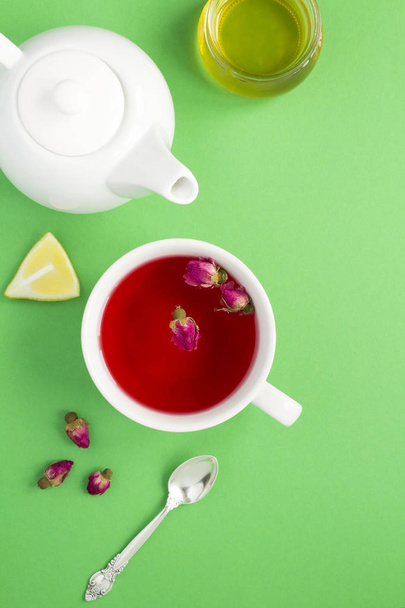 Φυτικό τσάι με ροζ τριαντάφυλλα στο λευκό κύπελλο στο πράσινο φόντο. Στο πάνω μέρος. Τοποθεσία ίλιγγος. Αντιγραφή χώρου. - Φωτογραφία, εικόνα