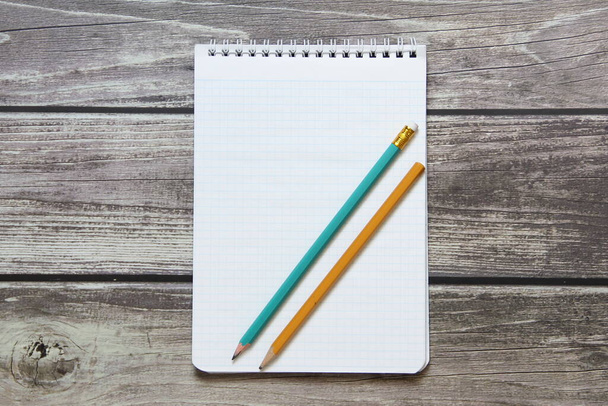 Bloc de notas con una hoja blanca en blanco en un papel de damero con lápiz de grafito simple se encuentra en el fondo de las tablas de madera
. - Foto, imagen