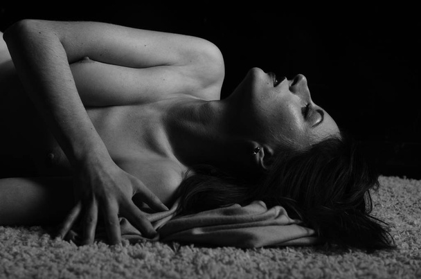 gyönyörű meztelen nő fekszik a borítón a sötét szobában  - Fotó, kép