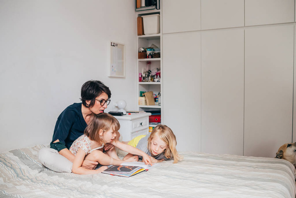 Мати двох дітей, які сидять на ліжку читають книгу, перемикається
 - Фото, зображення