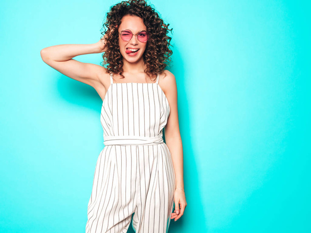 Portrait of beautiful smiling model with afro curls hairstyle dressed in summer hipster clothes.Sexy carefree girl posing near blue wall.Trendy funny and positive woman - Foto, imagen