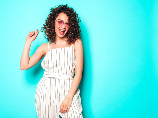 Portrait of beautiful smiling model with afro curls hairstyle dressed in summer hipster clothes.Sexy carefree girl posing near blue wall.Trendy funny and positive woman - Фото, изображение