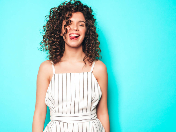 Portrait of beautiful smiling model with afro curls hairstyle dressed in summer hipster clothes.Sexy carefree girl posing near blue wall.Trendy funny and positive woman.Shows tongue - Foto, immagini