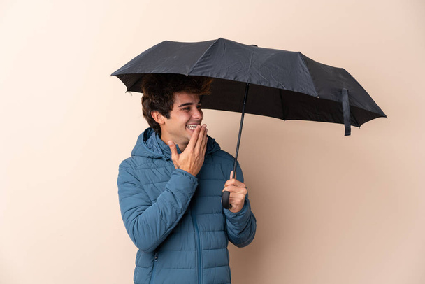 Homem segurando um guarda-chuva sobre fundo isolado com surpresa e expressão facial chocada
 - Foto, Imagem