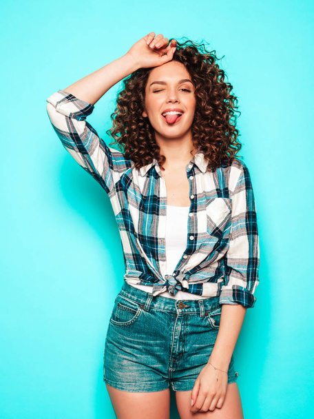 Portrait of beautiful smiling model with afro curls hairstyle dressed in summer hipster clothes.Sexy carefree girl posing in studio near blue wall.Trendy funny and positive woman - Photo, Image