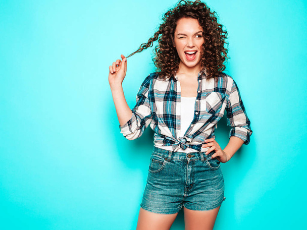 Portrait of beautiful smiling model with afro curls hairstyle dressed in summer hipster clothes.Sexy carefree girl posing in studio near blue wall.Trendy funny and positive woman - Fotó, kép
