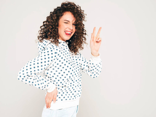 Portrait of beautiful smiling model with afro curls hairstyle dressed in summer hipster clothes.Sexy carefree girl posing on gray backgroundl.Trendy funny and positive woman in white hoodie - 写真・画像