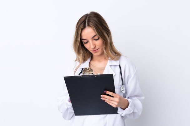 Young woman over isolated white background wearing a doctor gown and holding a folder - 写真・画像