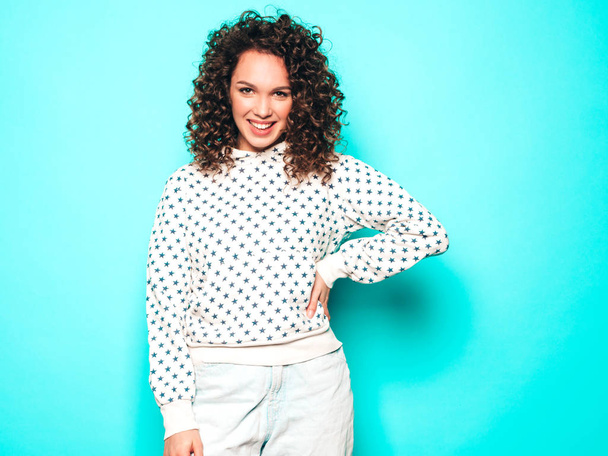 Portrait of beautiful smiling model with afro curls hairstyle dressed in summer hipster clothes.Sexy carefree girl posing near blue wall.Trendy funny and positive woman in white hoodie - Foto, Imagen