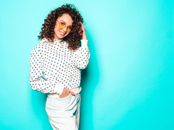 Portrait of beautiful smiling model with afro curls hairstyle dressed in summer hipster clothes.Sexy carefree girl posing near blue wall.Trendy funny and positive woman in white hoodie - Photo, image