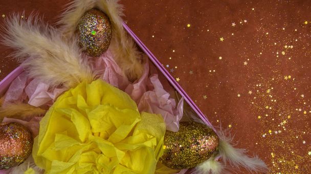 Paaseieren in een roze geschenkdoos met veren, paasversiering. Nest met gouden rode eieren op feestelijke rode achtergrond met glitters. Wenskaart. Vrolijk Pasen. - Foto, afbeelding