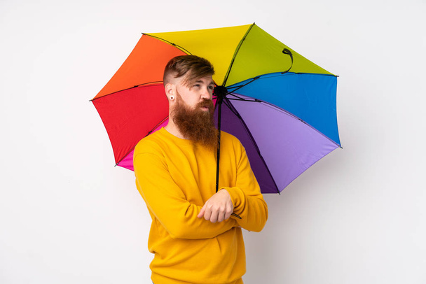 Κοκκινομάλλης με μακριά γενειάδα που κρατάει ομπρέλα πάνω από απομονωμένο λευκό φόντο και σκέφτεται μια ιδέα. - Φωτογραφία, εικόνα