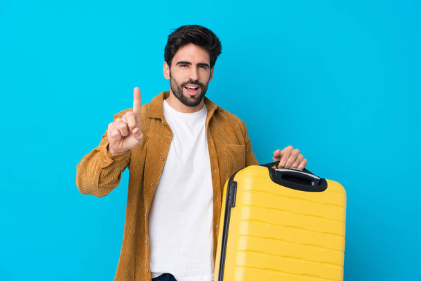 Giovane bell'uomo con barba su isolato sfondo blu in vacanza con valigia da viaggio e contando uno
 - Foto, immagini