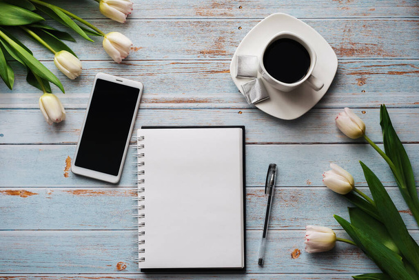 Primavera espacios en blanco de un lugar de trabajo freelancers con un ramo de tulipanes blancos, un teléfono inteligente, un ramo blanco vacío y una taza de café en sus manos sobre fondo de madera
 - Foto, imagen