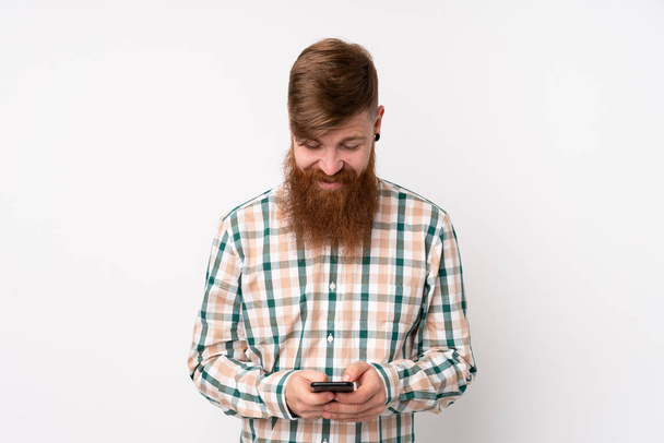 Redhead man with long beard over isolated white background sending a message with the mobile - Foto, Bild