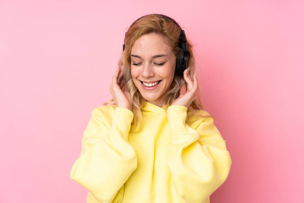 Giovane donna bionda indossa una felpa isolata su sfondo rosa musica d'ascolto - Foto, immagini