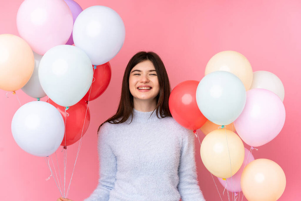 Молода українська дівчина - підліток тримає багато повітряних кульок над ізольованим рожевим фоном. - Фото, зображення