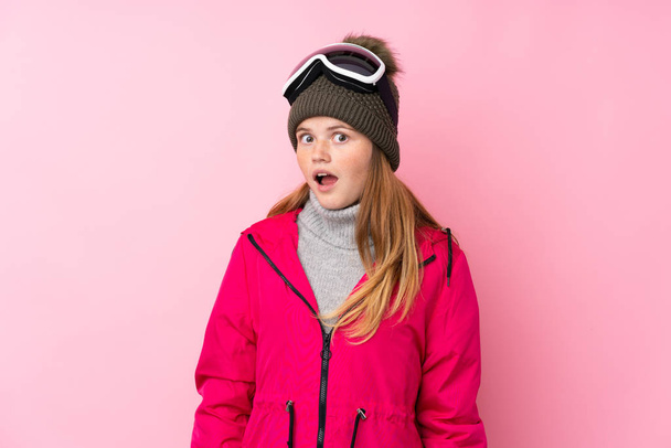 Українська дівчина-підліток з окулярами сноуборду над ізольованим рожевим фоном з несподіваним виразом обличчя. - Фото, зображення