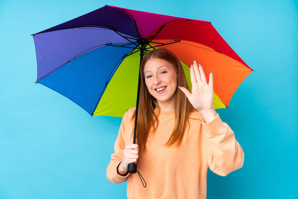Junge rothaarige Frau hält einen Regenschirm über der Mauer und grüßt mit fröhlichem Gesichtsausdruck - Foto, Bild