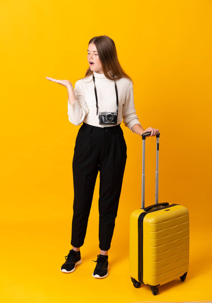 Volledig lichaam van reiziger tiener meisje met koffer over geïsoleerde gele achtergrond met copyspace imaginaire op de palm - Foto, afbeelding