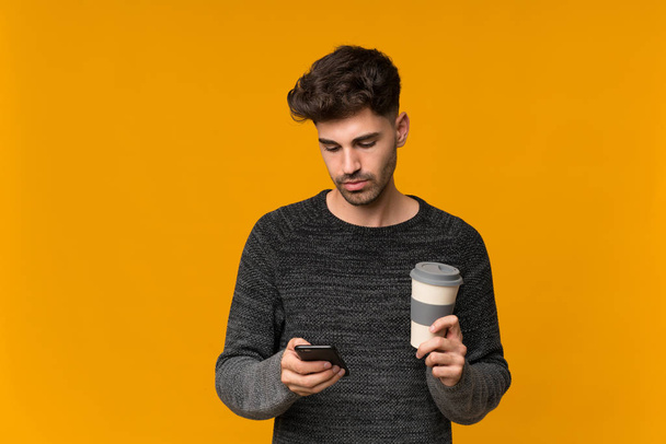 Jeune homme sur fond isolé tenant café à emporter et un mobile
 - Photo, image