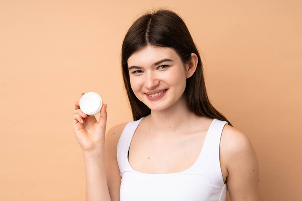 Young Ukrainian teenager girl over isolated background with moisturizer and happiness - Valokuva, kuva