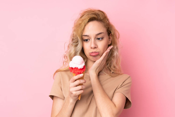 Joven rubia sosteniendo un helado de corneta aislado sobre fondo rosa - Foto, Imagen