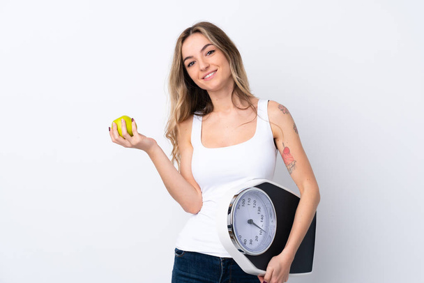 Young woman over isolated white background with weighing machine and with an apple - Fotografie, Obrázek