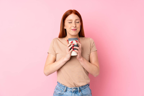 Молода руда жінка над ізольованим рожевим тлом тримає каву, щоб забрати
 - Фото, зображення