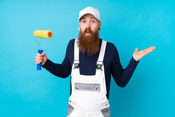 Homem pintor com barba longa sobre fundo azul isolado com dúvidas com expressão facial confusa
 - Foto, Imagem