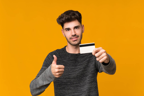 Young man over isolated background holding a credit card - Photo, Image
