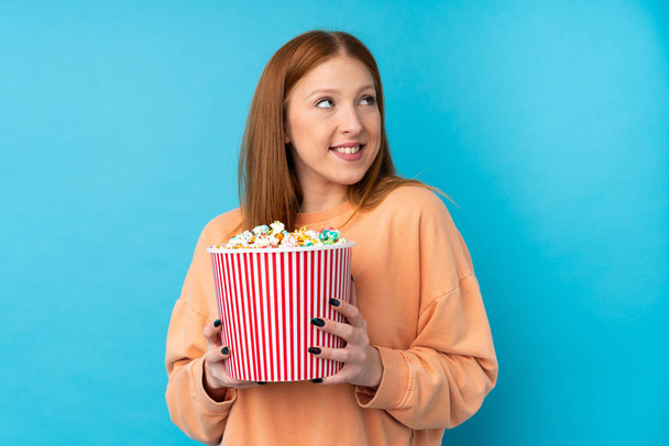 Jeune rousse femme sur fond isolé tenant un grand seau de popcorns - Photo, image