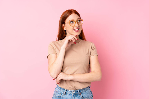 Молода руда жінка над ізольованим рожевим тлом в окулярах
 - Фото, зображення