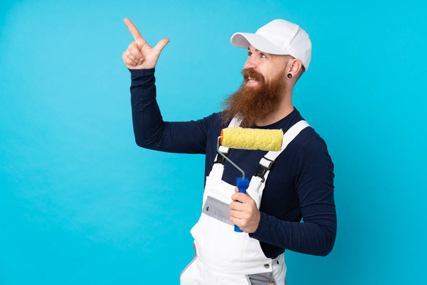 Schilder man met lange baard over geïsoleerde blauwe achtergrond wijzend met de wijsvinger een geweldig idee - Foto, afbeelding